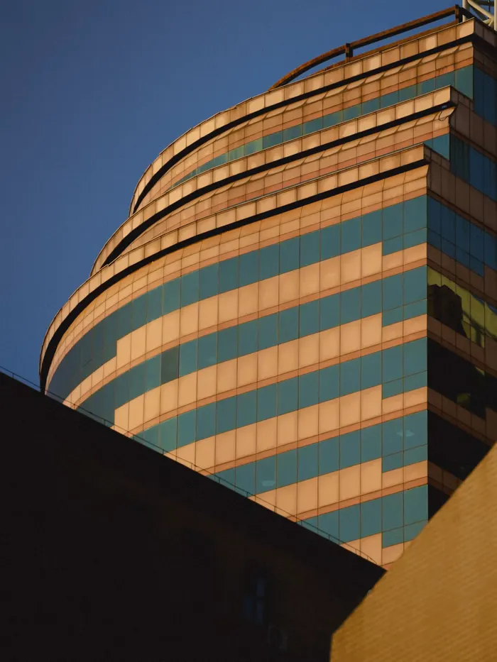 A curved glass office tower seen from below in late afternoon light.