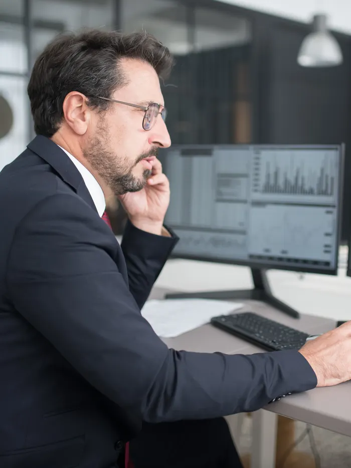 A trader at a desk, hand on the mouse, reading charts across two screens.